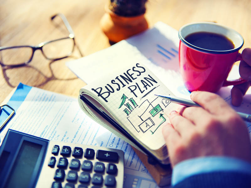 Buch mit Businessplan, Kaffeetasse und Taschenrechner auf Tisch